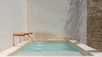 Una piscina rectangular con agua que fluye desde un caño de bambú.