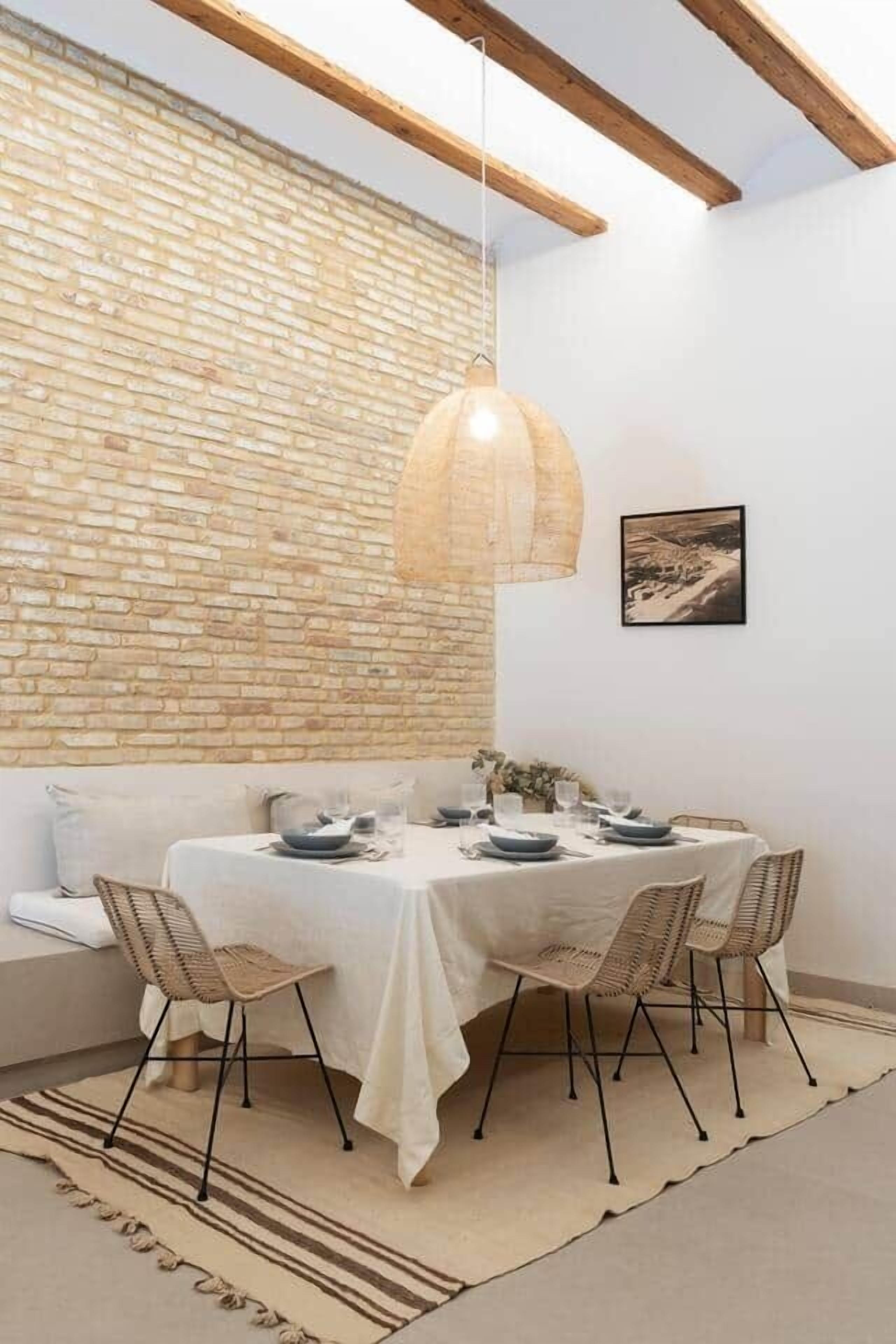 Un comedor con pared de ladrillo, lámpara colgante, mesa dispuesta con platos y vasos, y un sofá.