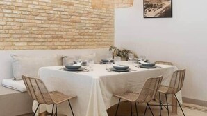 Uma sala de jantar com parede de tijolos, luminária pendente, mesa posta com pratos e copos, e um sofá.