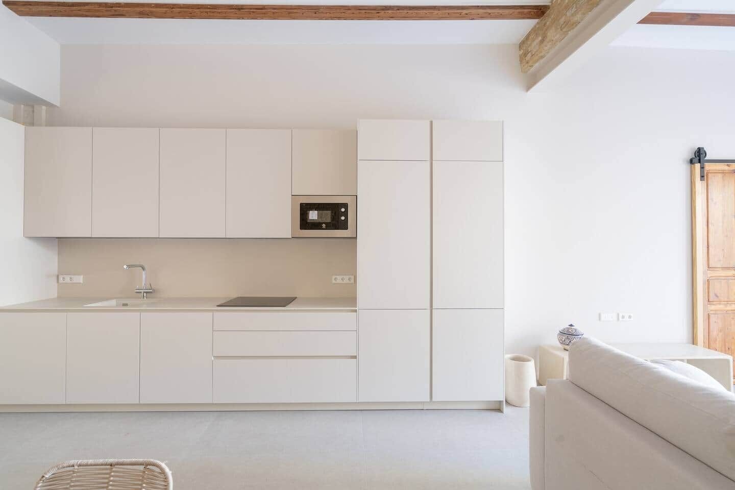 Una cocina moderna con armarios blancos, horno empotrado y lavamanos.