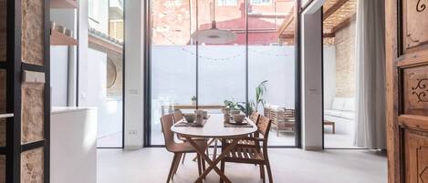 A dining area with a round table, chairs, and a view through large glass doors to an outdoor space.