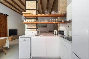 A compact kitchen with white cabinetry, a dishwasher, a microwave, and a sink. There are shelves above the sink holding glassware. - ⭐️NEW⭐️ PATIO A HOUSE. Walk to Beach, port & Met (Valencia)