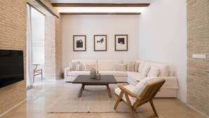 Una sala de estar moderna con un sofá blanco, una mesa de centro de madera y un televisor montado en la pared.