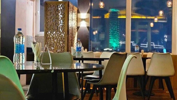 A restaurant with a view of a cityscape at night, modern furniture, and a decorative wall.