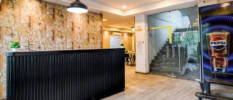 A reception area with a patterned wall, a black reception desk, a hanging light fixture, and a glass door leading to a staircase.