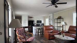 A spacious living area with a dining table, two leather chairs, a sofa, a coffee table, and a kitchen in the background. - Cozy & quiet 2 bedroom country getaway, close to all the fun! (Elberta)