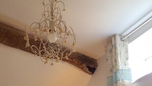 Ein Zimmer mit einer Chandelier, einem fensterbelaubten Fenster, einem Wandbild und einer Nachttischlampe.