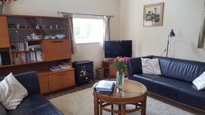 Ein Wohnzimmer mit einer Couch, einem Couchtisch mit einem Buch und Blumen, einem Fernseher und einem Bücherregal mit Büchern und Dekoration.