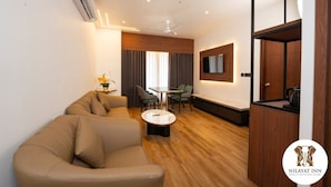 A modern hotel room with a sofa, a small table, a TV, and a wooden cabinet. - NILAYAT INN (Thrissur)