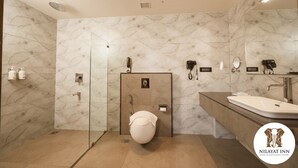 A modern bathroom with a marble wall, a glass shower enclosure, a toilet, a sink, and a mirror. - NILAYAT INN (Thrissur)