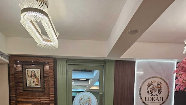 A lobby with a marble floor, a framed picture on the left, a sofa on the right, and a Lokah logo on the wall. - NILAYAT INN (Thrissur)