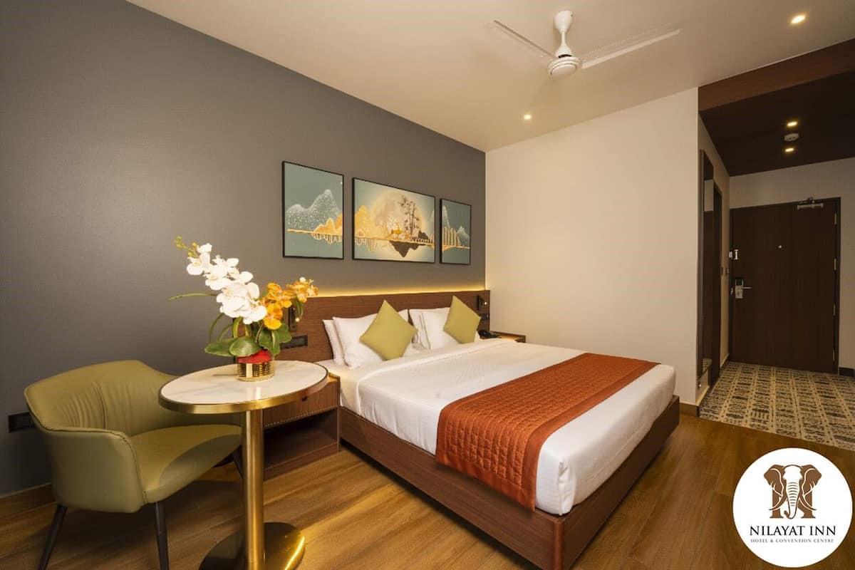 A hotel room with a bed, a round table with a vase of flowers, a green armchair, and three framed pictures on the wall.