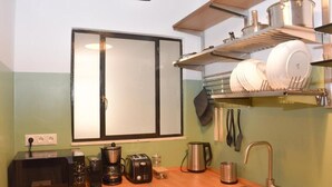 Cocina pequeña con microondas, tostadora, cafetera y hervidor sobre la encimera. También se ve un lavabo y una ventana con persianas.