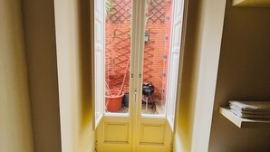 Un pasillo estrecho con piso amarillo que conduce a un par de puertas dobles, desde donde se ve una pared de ladrillo y un pequeño jardín exterior.
