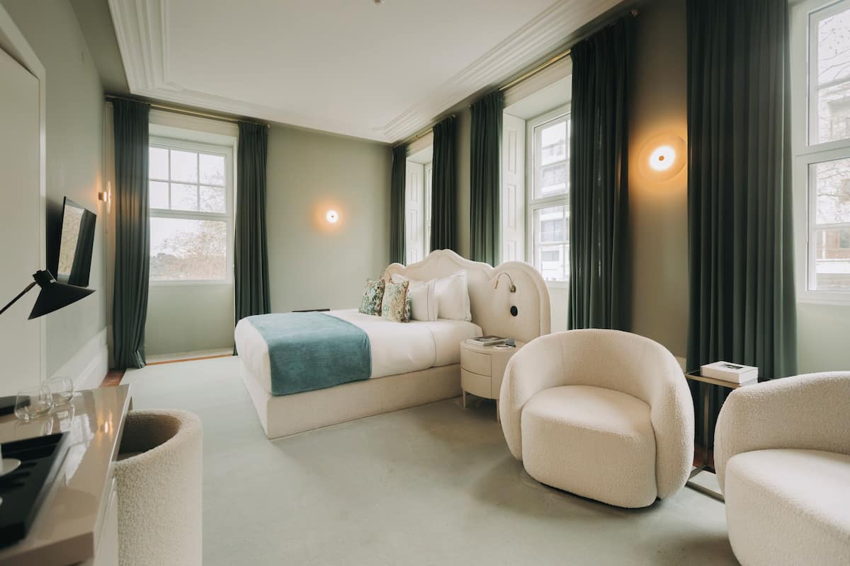 A spacious bedroom with a large bed, a bedside table, a chair, and a desk with a lamp.