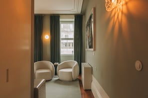 Un couloir avec deux fauteuils, un radiateur et une fenêtre avec des rideaux.