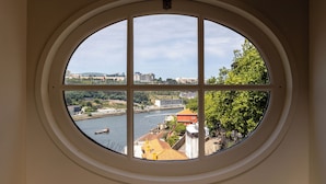 A round window with a view of a river, buildings, and greenery. - Torel Private Collection (Porto)
