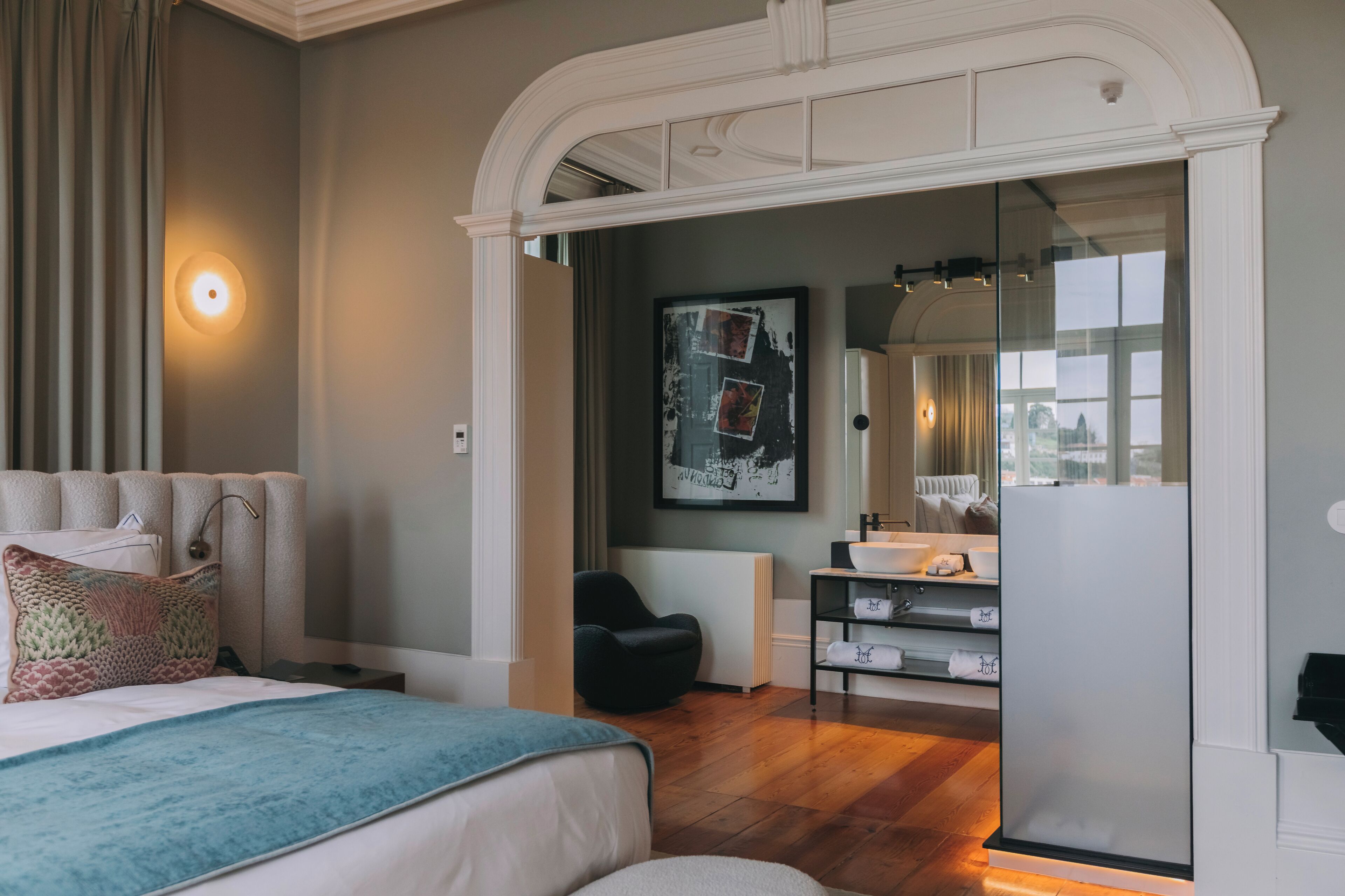 Habitación de hotel moderna con una cama grande, zona de estar, baño con espejo amplio y vista a la ciudad.