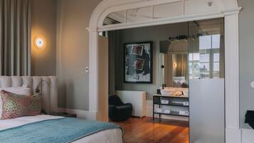 Habitación de hotel moderna con una cama grande, zona de estar, baño con espejo amplio y vista a la ciudad.