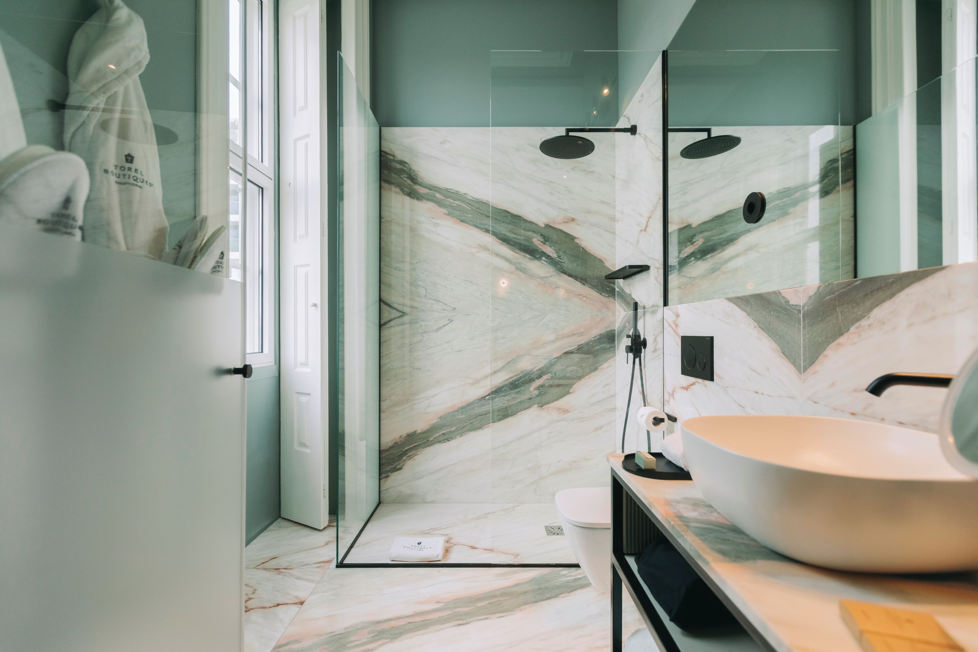 Un bagno moderno con cabina doccia in vetro, lavabo bianco e pannello di schienale in marmo.