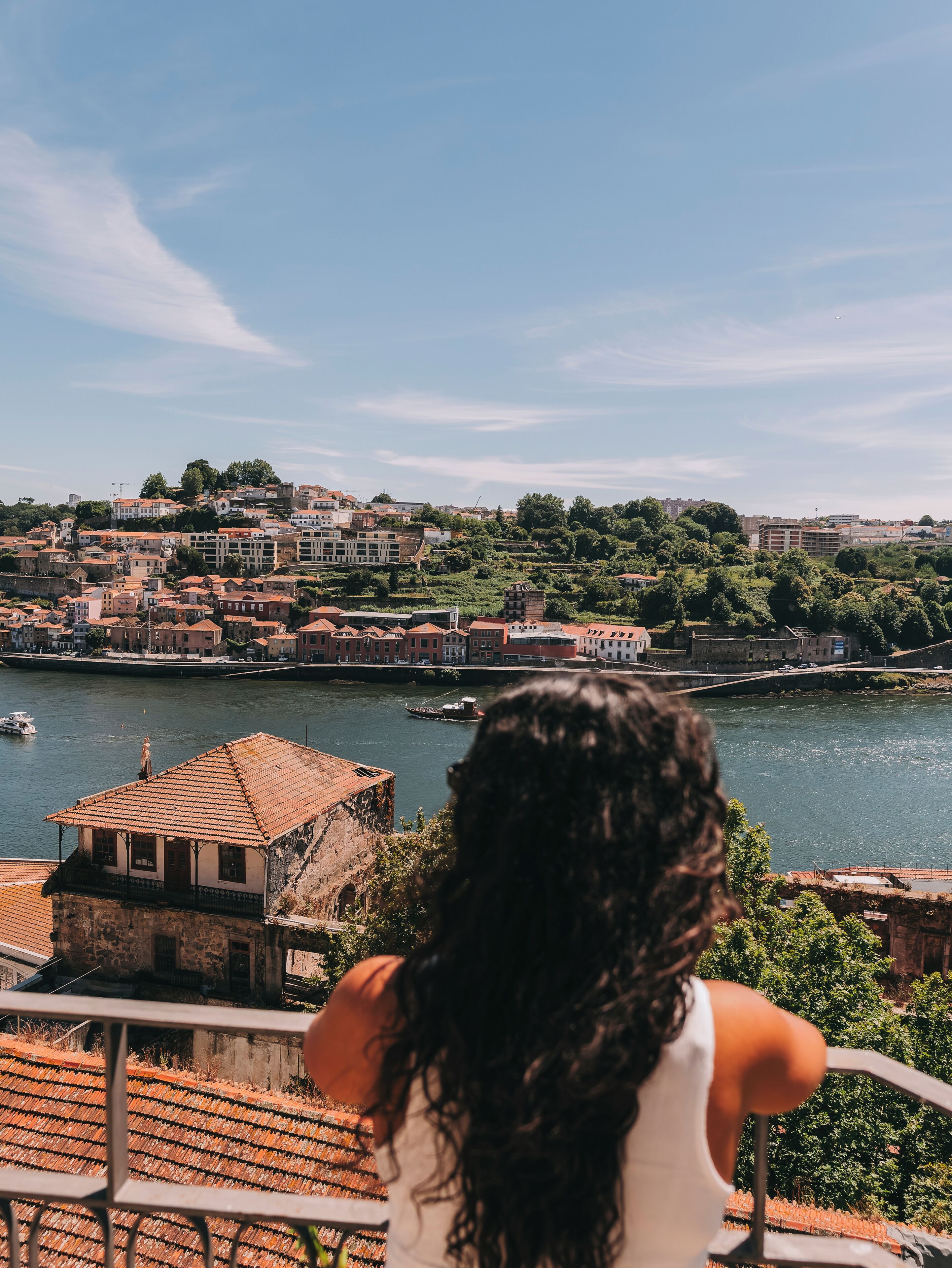 Uma pessoa admirando uma cidade ribeirinha com edifícios históricos e vista para o rio.