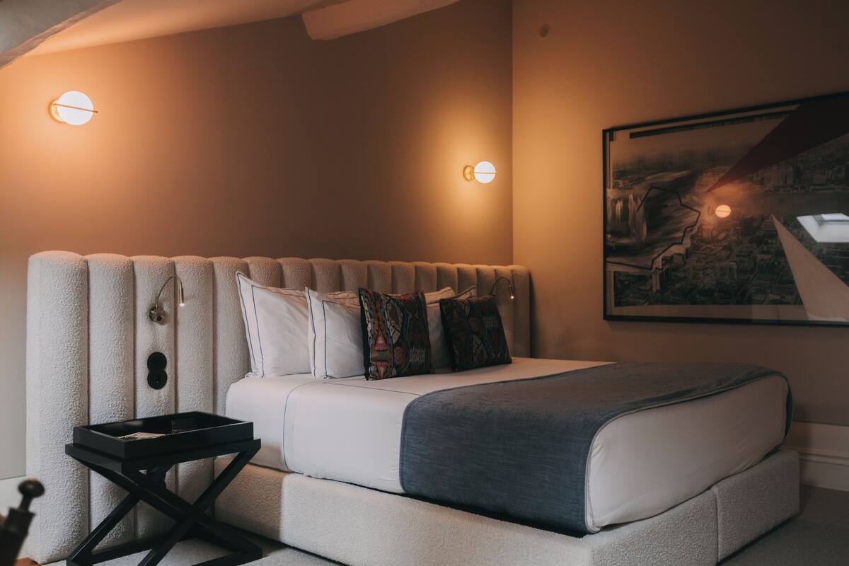 A modern bedroom with a large bed, a bedside table, and a wall-mounted light fixture.
