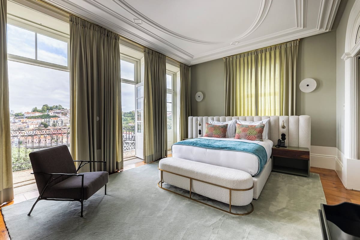A spacious bedroom with a large bed, a chair, and a view of the city through large windows.