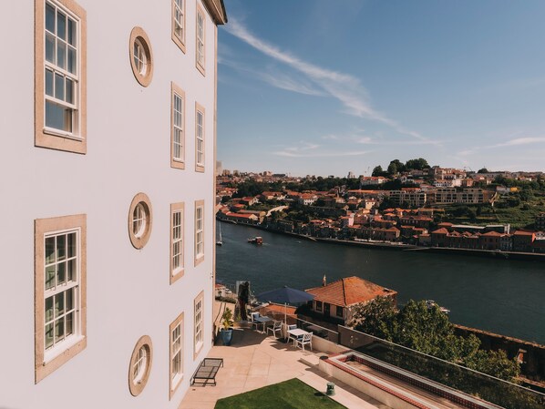 A building with multiple windows and a balcony overlooking a river with boats. - Torel Private Collection (Porto)