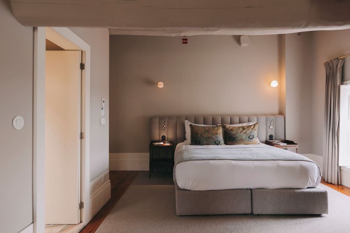 A bedroom with a bed, bedside tables, a nightstand, a wall-mounted light, and a door.