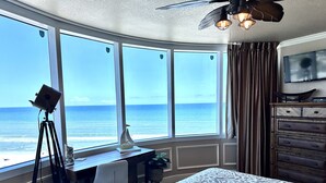 Ein Schlafzimmer mit großem Fenster und Blick auf den Ozean, einem Schreibtisch mit Teleskop und einem Bett mit gemustertem Überwurf.