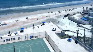 Blick auf einen Strand mit Tennisplatz, Sonnenschirmen und Liegestühlen.