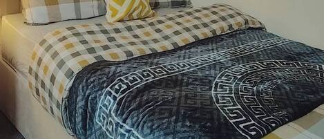 A bed with a checkered bedspread, a patterned throw blanket, and multiple pillows.