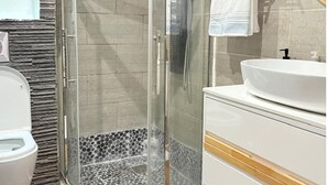 Ett badrum med en dusch som är avskärmad med glasväggar, ett vitt handfat och en toalett.