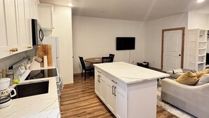 A modern kitchen with white cabinetry, a marble countertop, and a dining area with a table and chairs.