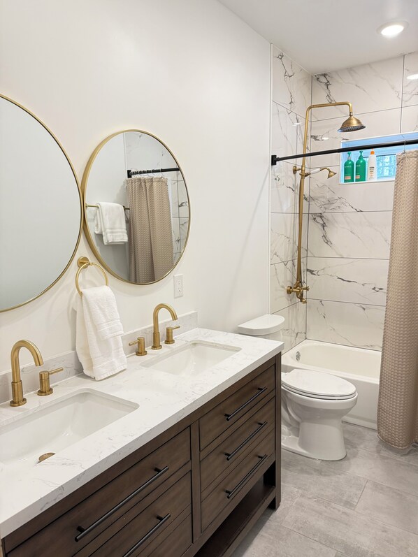 A modern bathroom with two sinks, a toilet, a bathtub, and a shower.