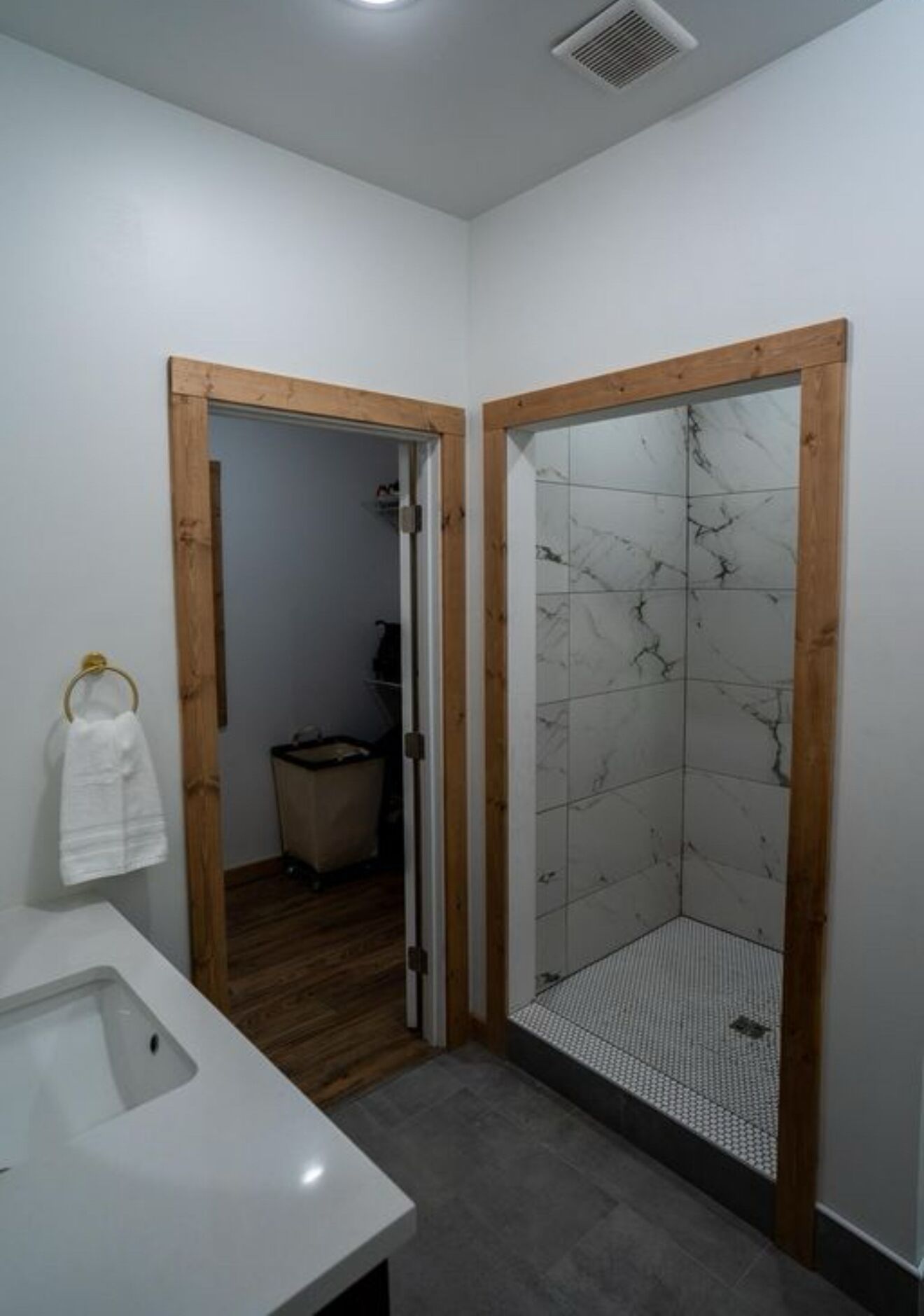 Une salle de bain avec un lavabo blanc, des cadres de porte en bois et une douche avec un mur carrelé.