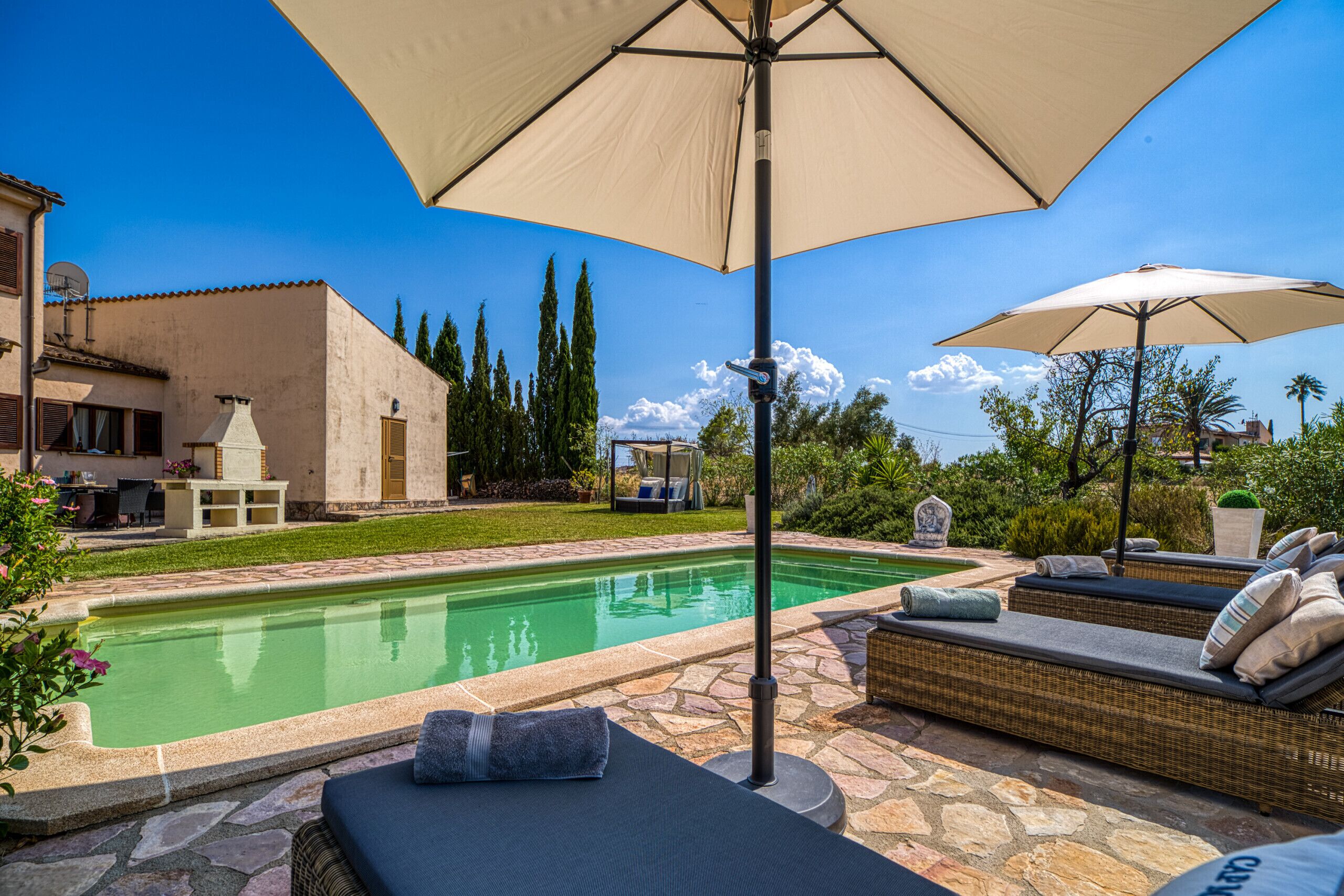A swimming pool with lounge chairs and umbrellas, surrounded by stone tiles and greenery.