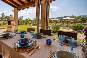 Un espace de restauration en plein air avec une table dressée pour quatre personnes, entourée de chaises, et offrant une vue sur une piscine et un jardin.