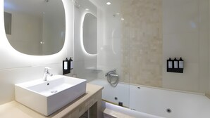 Un bagno moderno con un grande specchio ovale, un lavabo rettangolare, una doccia con pareti in vetro e un portalampada fissato alla parete.