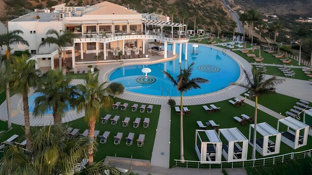 Un resort con una grande piscina centrale, diverse zone relax e un edificio con balconi vista piscina.