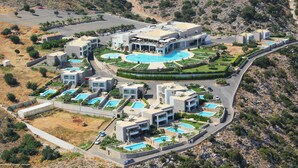 Un resort moderno con diverse piscine, un edificio centrale con tetto curvo e uno sfondo montuoso.