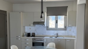 A modern kitchen with a glass dining table, white cabinets, and a built-in oven. - Villa 'One Bedroom Villa with Pool View' with Wi-Fi and Air Conditioning (Malia)