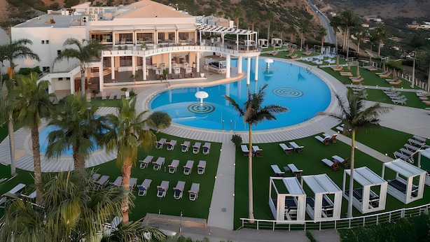 A resort with a large pool, sun loungers, and a building with multiple balconies. - Villa 'One Bedroom Villa with Pool View' with Wi-Fi and Air Conditioning (Malia)