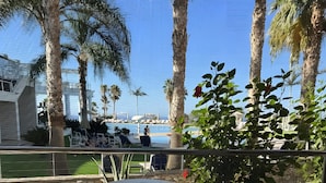 A terrace with two plastic chairs, a round table, and a view of a pool and palm trees. - Villa 'One Bedroom Villa with Pool View' with Wi-Fi and Air Conditioning (Malia)