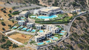 A modern resort with multiple swimming pools, a central building with a curved roof, and a mountainous backdrop. - Villa 'One Bedroom Villa with Pool View' with Wi-Fi and Air Conditioning (Malia)