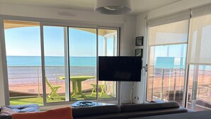 Quarto com grande janela com vista para a praia, televisão de tela plana na parede e piso de madeira.