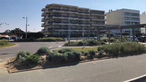 Um edifício residencial com vários andares, varandas, área de estacionamento e canteiro central ajardinado.