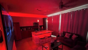 A modern living room with a red-lit ambiance, a central island with bar stools, a sofa, and a coffee table. - Cozy 1-Bedroom Studio in Tranquil Atlanta (Atlanta)