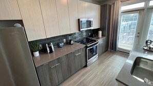 A modern kitchen with a built-in microwave, stove, and oven, wooden cabinets, and a large window with blinds. - Cozy 1-Bedroom Studio in Tranquil Atlanta (Atlanta)