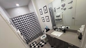 A bathroom with a checkered shower curtain, a toilet, a sink with a mirror, and a towel rack. - Cozy 1-Bedroom Studio in Tranquil Atlanta (Atlanta)